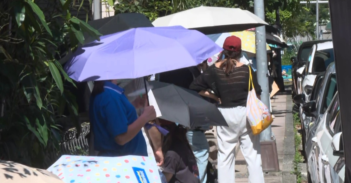 17日一早，北市大安區街頭，長長人龍，頂著33度高溫，撐著洋傘蹲坐路邊。（圖／東森新聞）